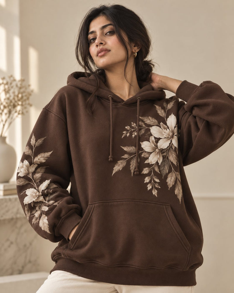 Woman in a brown hoodie with a cream floral print across the front and sleeve